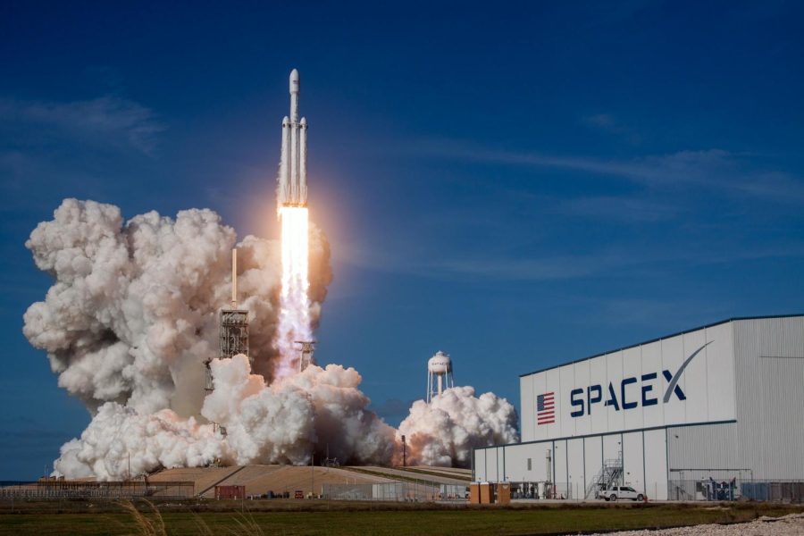 One of SpaceX’s rockets, Falcon Heavy, takes off for a demo mission in front of a building labeled “SpaceX.”
