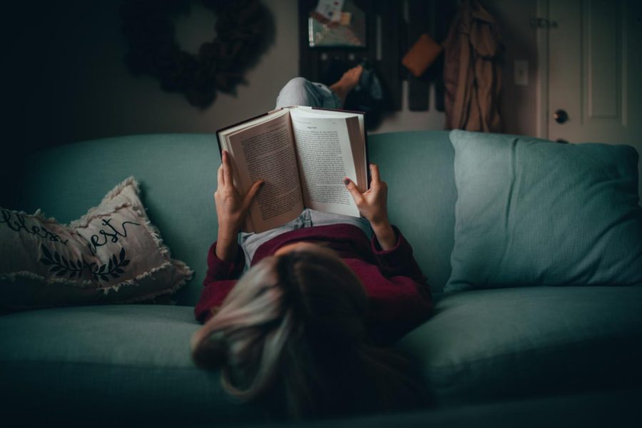Girl sitting on the couch attempting to read a book for school.